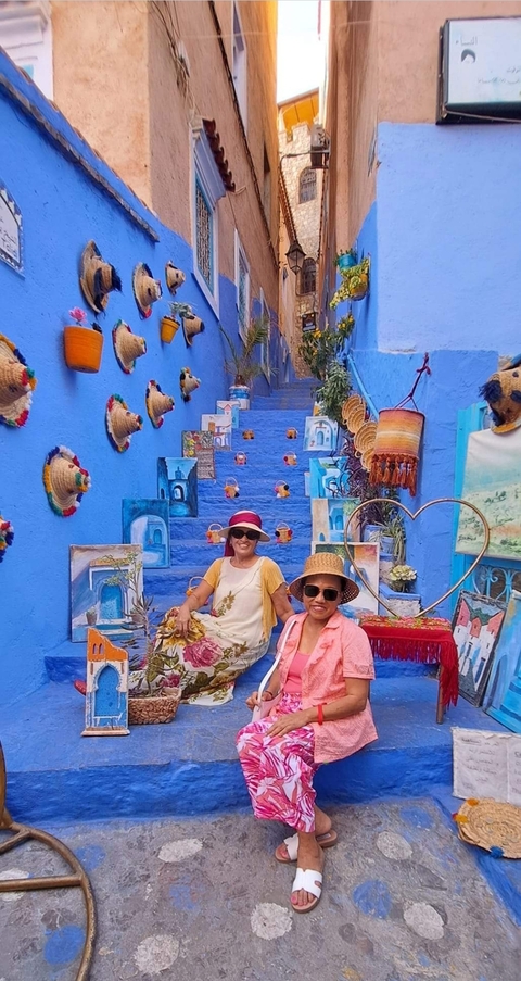 Two women sitting on blue stairs decorated with local crafts.