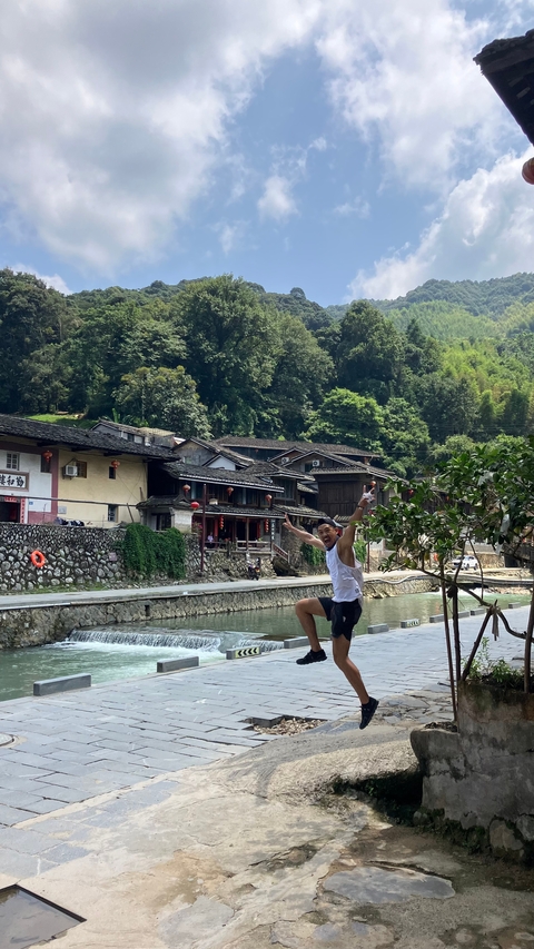 Person joyfully jumping in front of traditional Chinese buildings near a river.