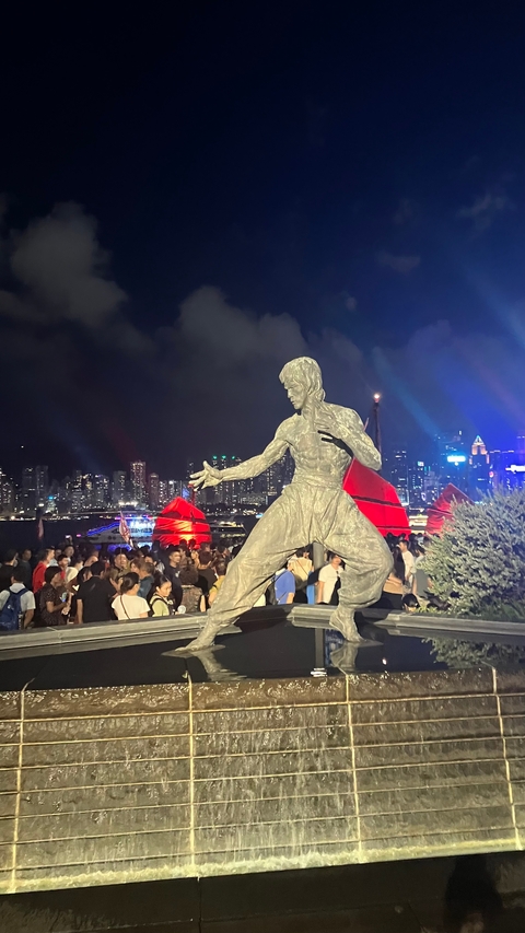 A statue of a martial arts icon in a crowded nighttime urban setting.
