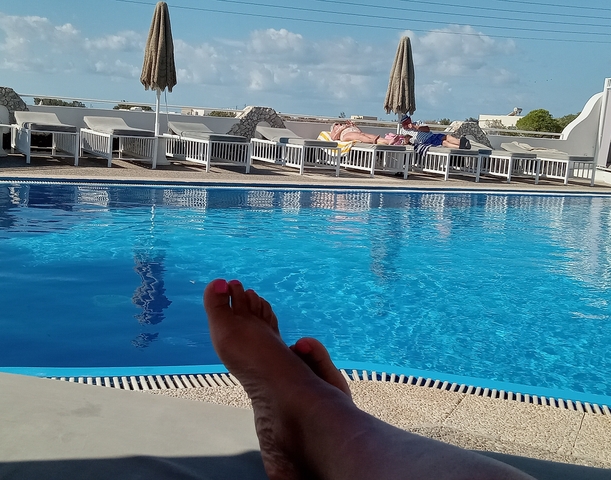 View from a pool with toes in view, overlooking sunbeds.
