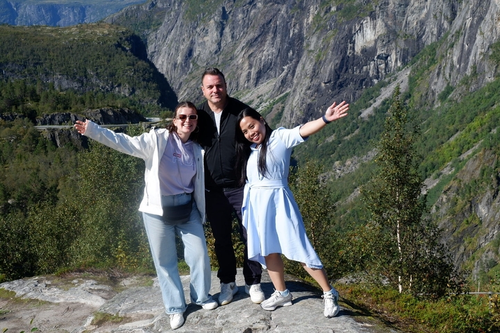 Three people posing with arms wide open in front of mountainous terrain.