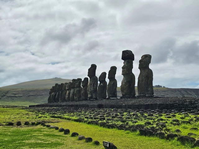       Line of Moai statues on a stone platform with hilly terrain.
  