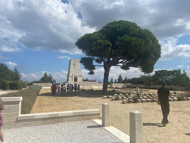 Tour group gathered near a historical monument in a park-like setting.