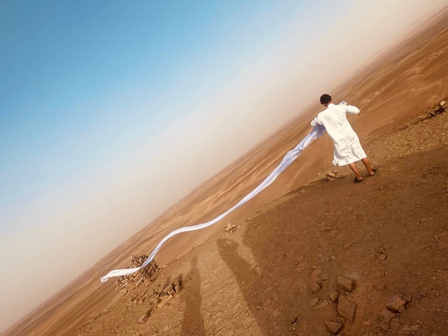 Person in white clothing with a long scarf standing on a desert hill.