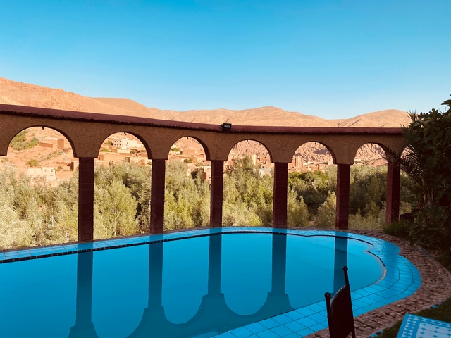 View of a swimming pool framed by arches with a mountainous backdrop.