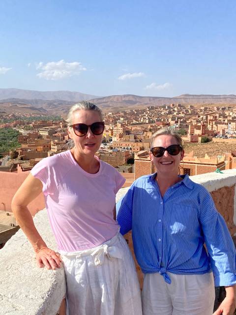       Two women posing on a rooftop with a view of a town.
  