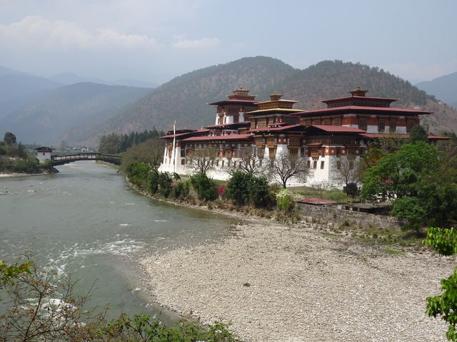      Dzong beside a river with mountains in the background.
  