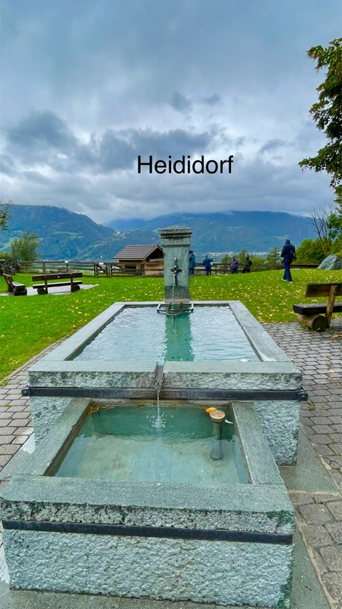A stone fountain with people in the background in a mountain setting.