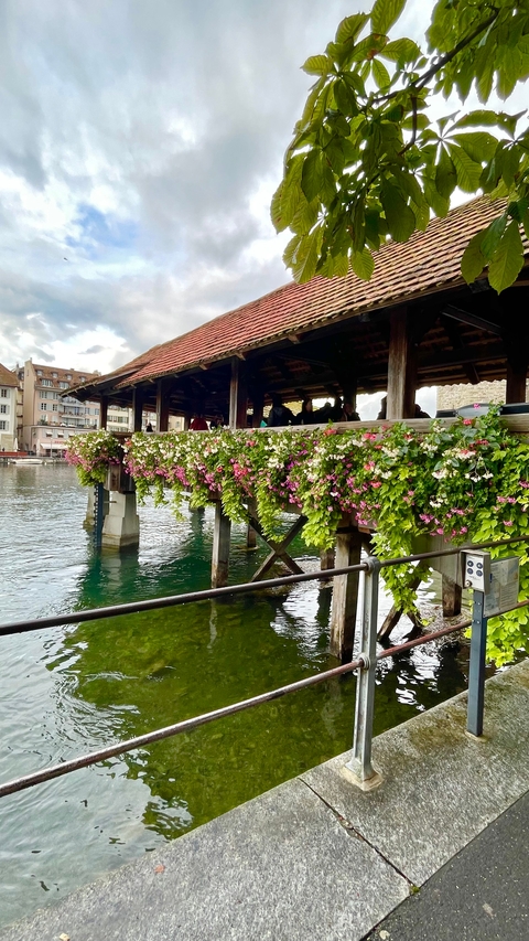 Covered wooden bridge adorned with flowers over a river.