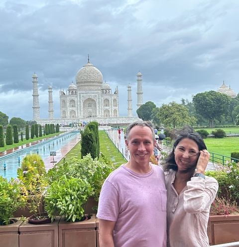       Couple smiling with the Taj Mahal in the background on a cloudy day.
  