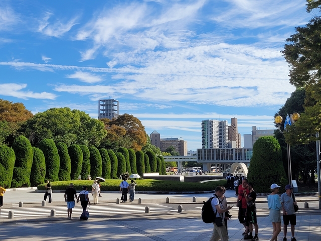       Beautiful park with people walking, trees, and cityscape under a clear blue sky.
  