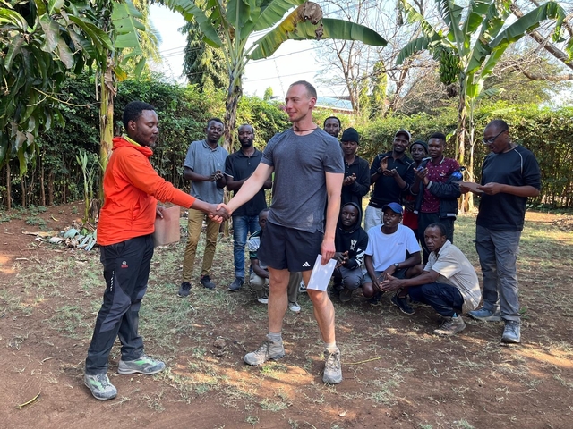       People gathered outdoors, two shaking hands, in a group setting.
  