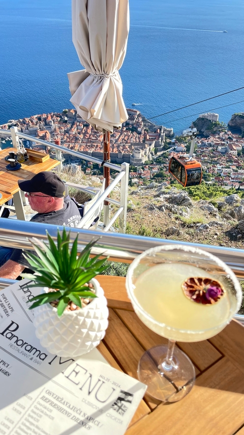 A man enjoying a drink with a view of a cable car and city below.