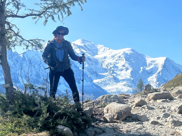 Hiker posing with trekking poles and snowy peaks in the background.