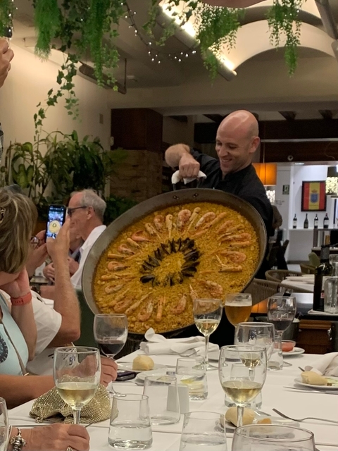 Chef serving a large paella dish at a restaurant.