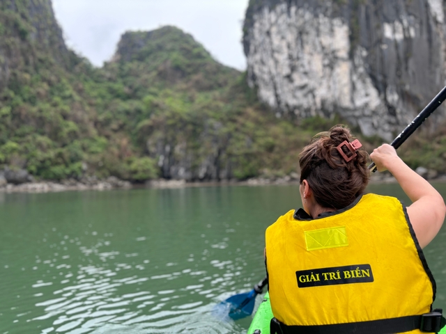 Person paddling a boat in a scenic water body with cliffs in the background.