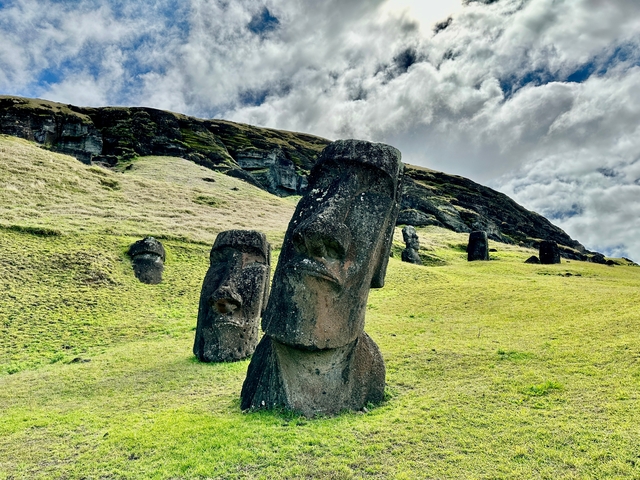 Statue heads partially buried in the ground with hill backdrop.