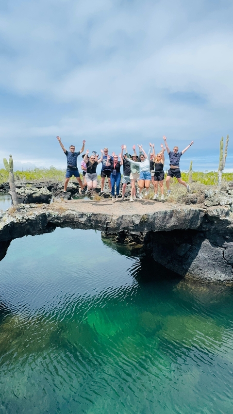 A group jumps on rocky terrain with cacti around.