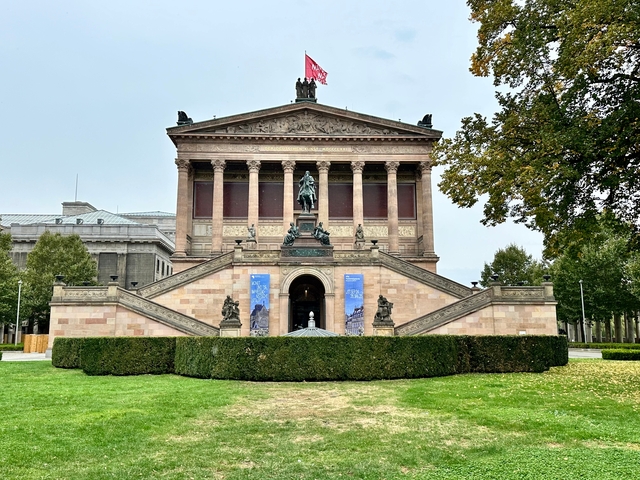       Neoclassical building with a statue in front.
  