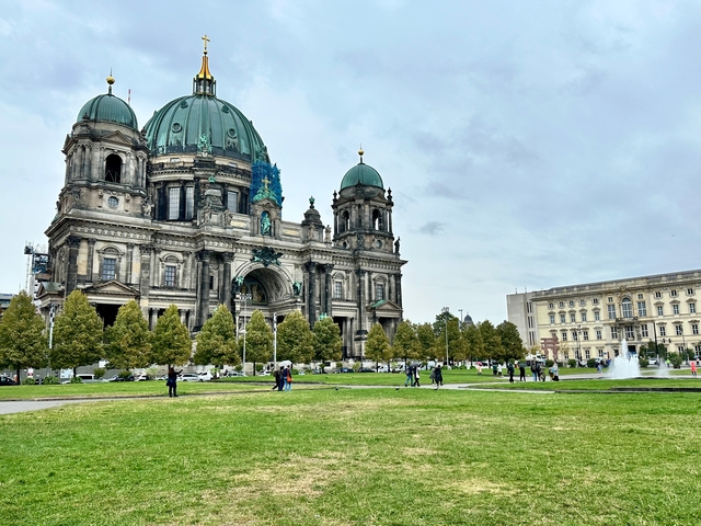       Large domed cathedral with people and a grassy park.
  
