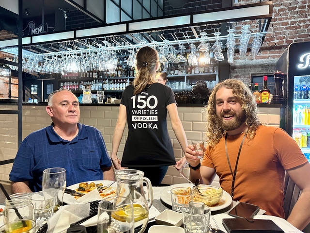       Group enjoying a meal with a person wearing a shirt with text.
  