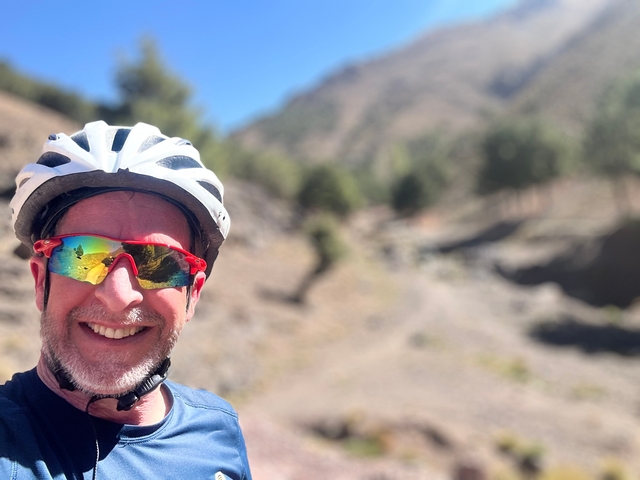 A person in cycling gear taking a selfie in a mountainous area.