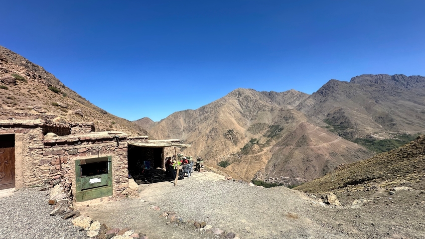 A small stone hut on a mountain trail with a vast valley view.