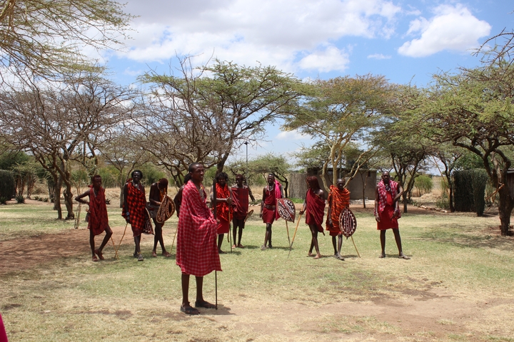 A group of Maasai people standing outdoors with trees and a bright blue sky.