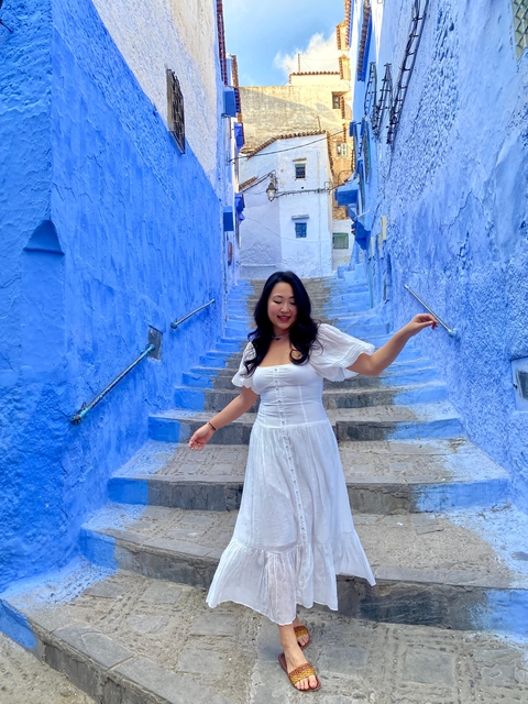 Woman in white dress on blue-washed stairs in a Moroccan city.