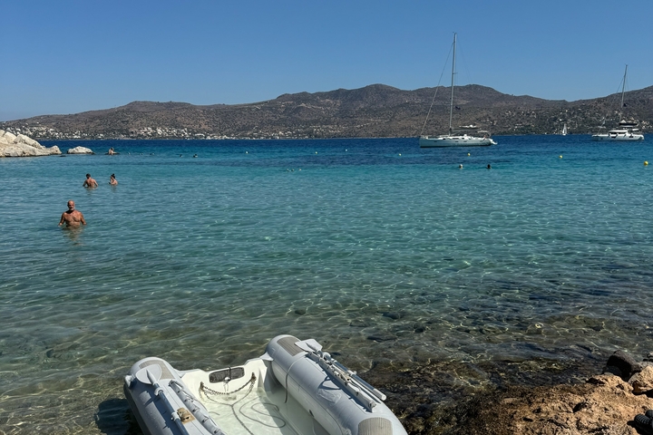       Calm beach with clear water and yachts anchored nearby.
  