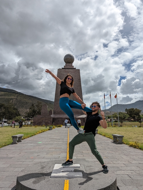 Two people jumping in front of Mitad del Mundo monument.
