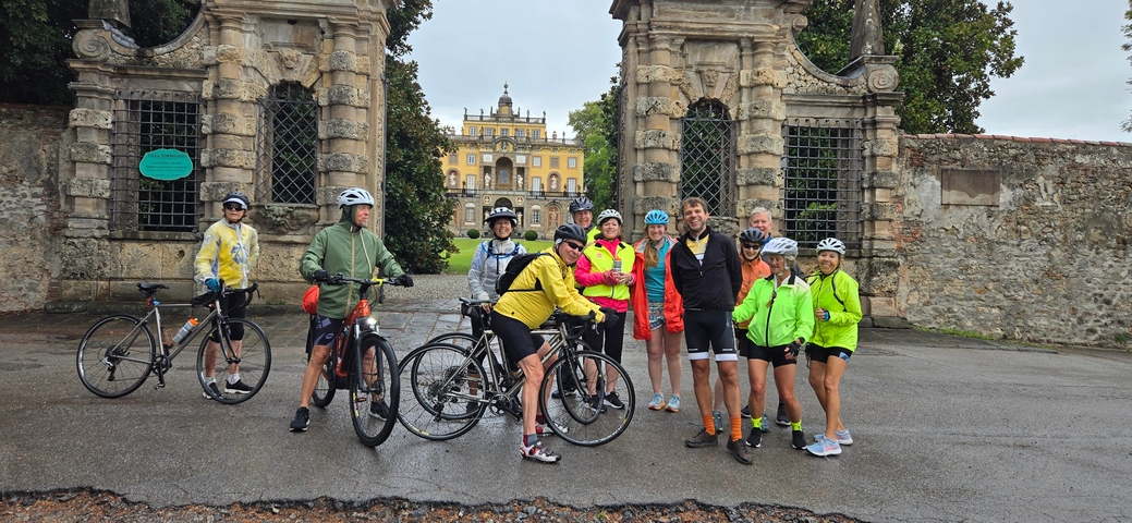       A group of cyclists posing in front of an ornate gate with a historic building in the background.
  