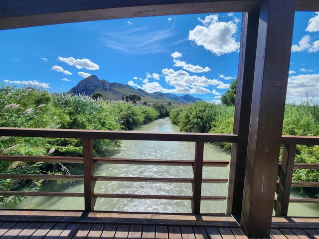 Wooden bridge over a river with mountains and blue sky