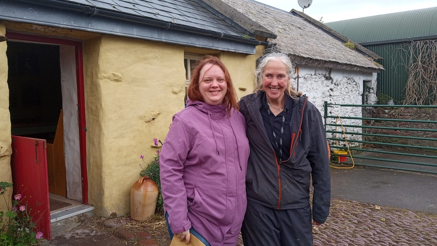       Two women standing outside a traditional Irish cottage.
  