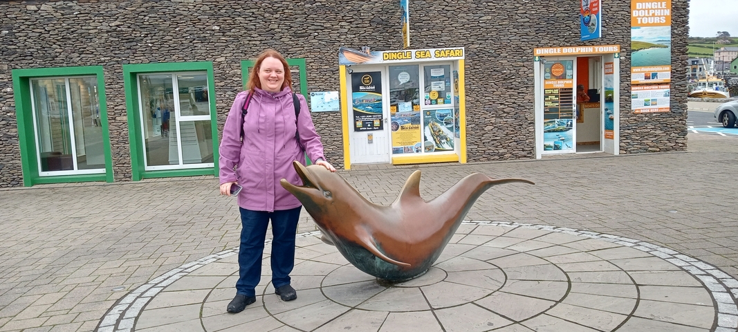       A person standing by a statue of a dolphin.
  