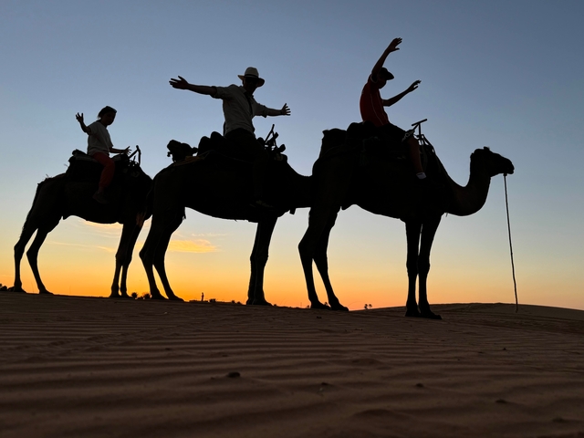       Silhouette of people riding camels at sunset.
  