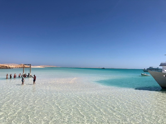 People enjoying the beach with a boat in the clear blue water.