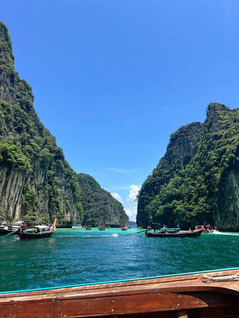       Sheer limestone cliffs draped in jungle tower toward a bright blue sky over a narrow waterway.
  