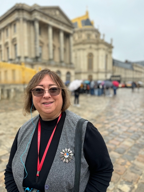       A woman smiling with a blurred background showing people and architecture.
  