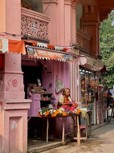 An elderly woman sitting outside a colorful shop with vibrant decorations.