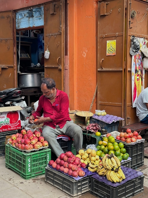 A fruit vendor arranging apples on the street with colorful stalls around.
