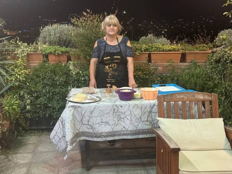       A woman standing at a table outdoors with cooking materials.
  