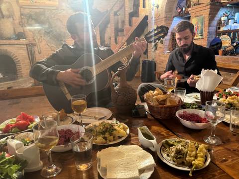       Two musicians playing instruments over a dinner table with food.
  