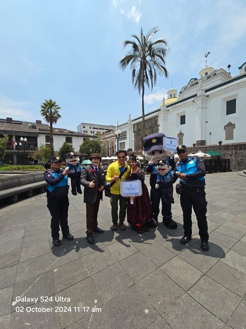 Group of people including police officers and mascots posing for a photo in a city square.