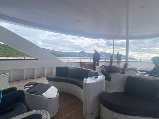 People on a yacht deck with mountainous landscape in the background.