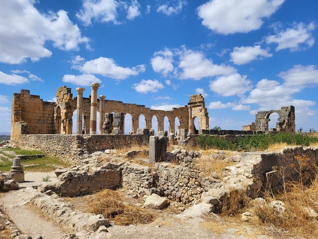       Ruins of ancient Roman architecture under a blue sky.
  