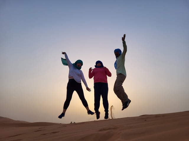       Three people wearing scarves jumping in a desert at sunset.
  