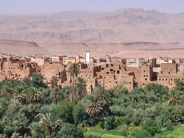       A scenic view of traditional adobe buildings with a lush foreground and arid mountains in the background.
  