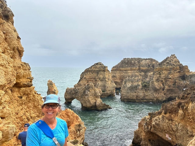 Person smiling in front of coastal rock formations by the sea