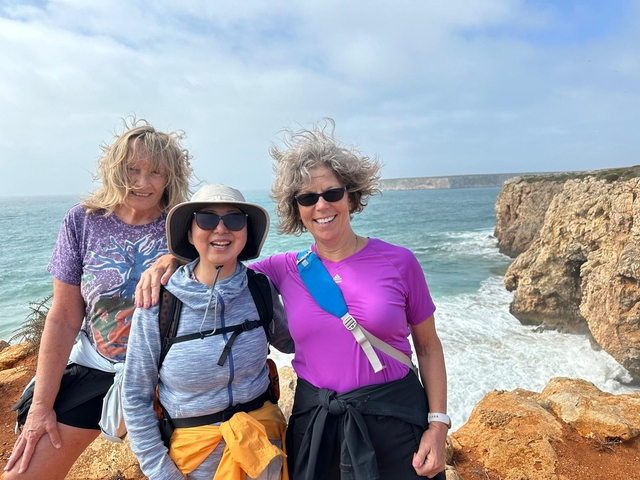 Three women posing on a rocky coast with rough seas